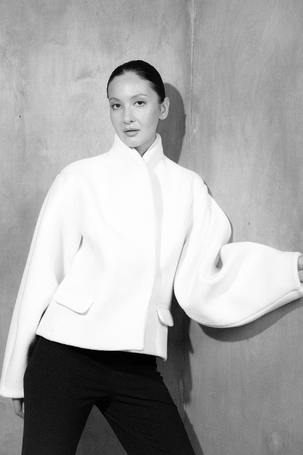 Alen wool jacket in ivory, one arm held out against a grey wall