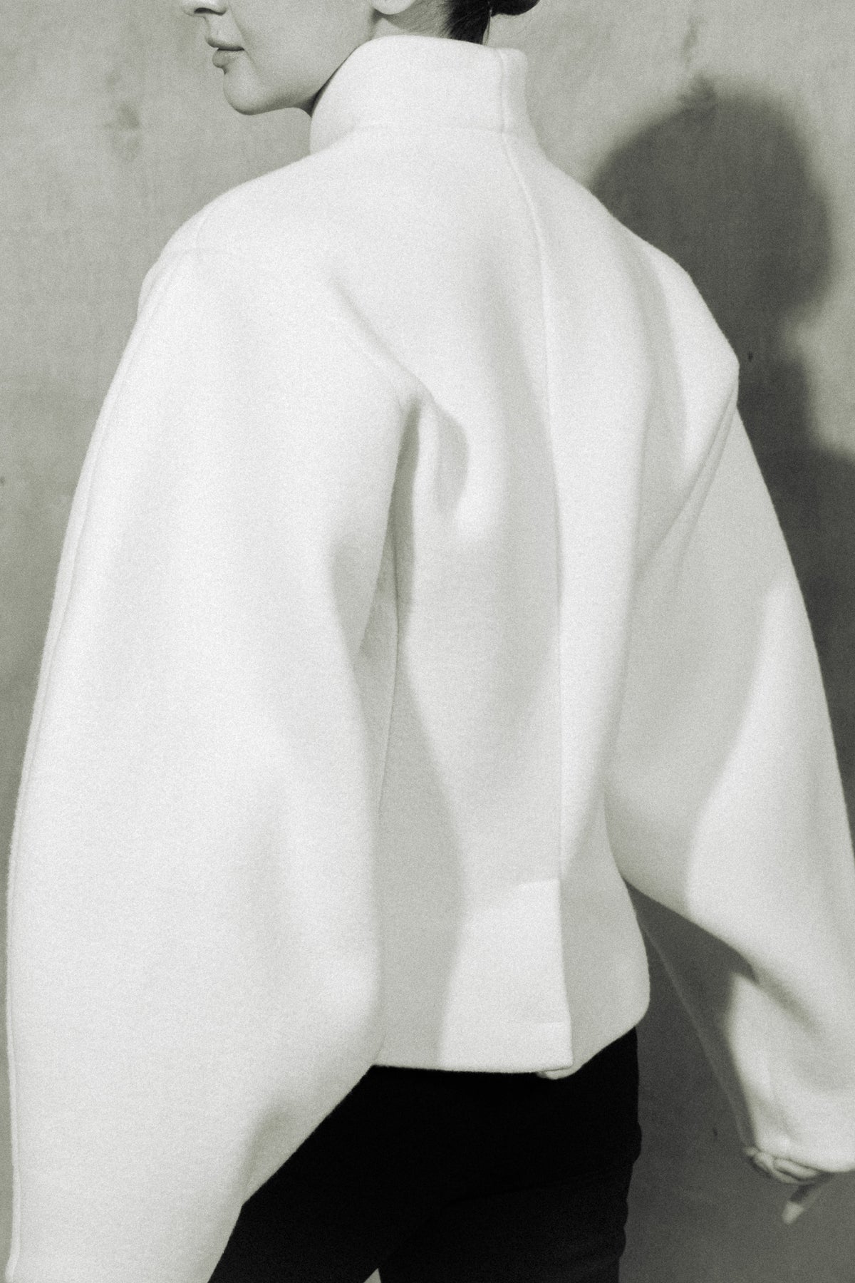Alen wool jacket in ivory, the rounded sleeve in profile against a grey wall