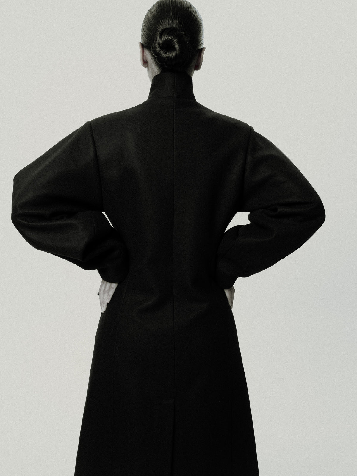 Long black wool coat seen from behind, hands on the hips