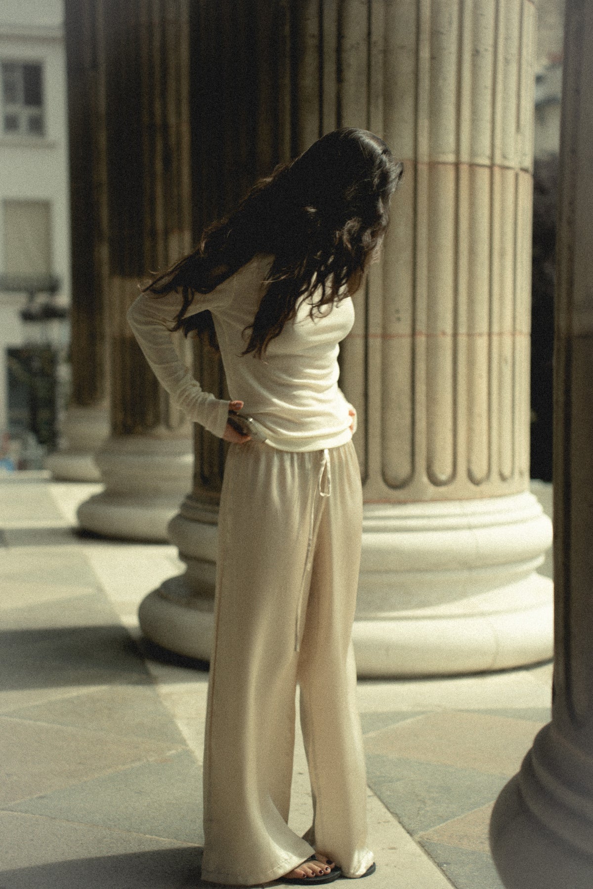 Pantalon en soie champagne à jambe large, près des colonnes de pierre à Paris, le regard baissé