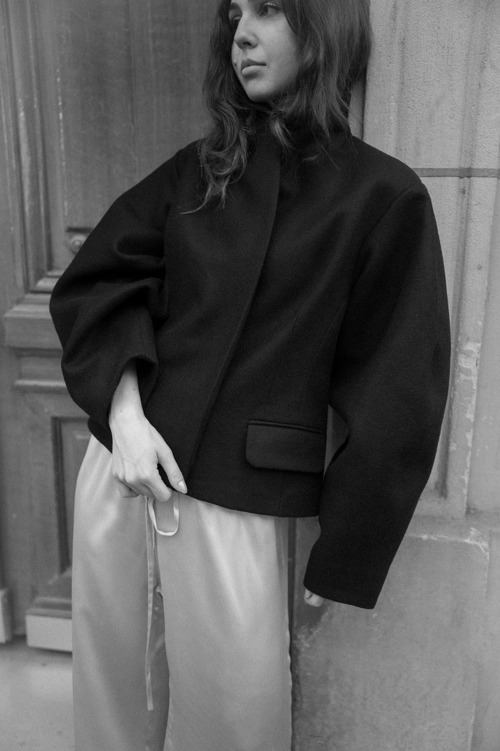 Fitted balloon-sleeve wool jacket in black, worn with silk trousers, black and white street photograph