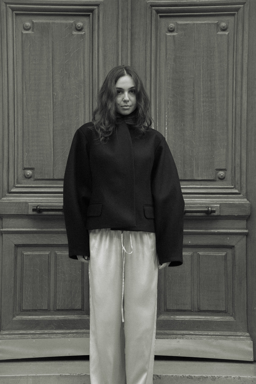 Fitted balloon-sleeve wool jacket in black, in front of a carved wooden door, black and white