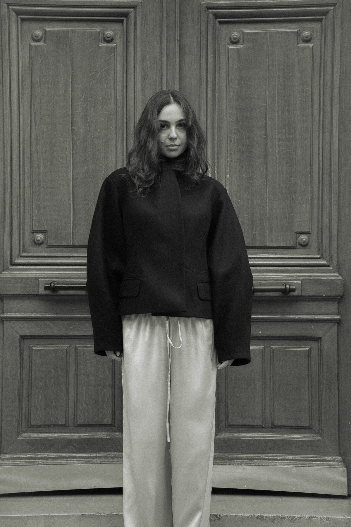 Fitted balloon-sleeve wool jacket in black, in front of a carved wooden door, black and white